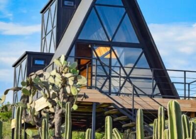 Cabaña A-frame de metal negro iluminada de noche, estilo sugerido Paraíso Escondido
