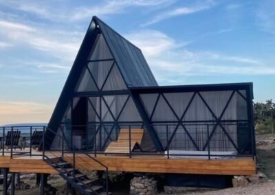 Cabaña A-frame de metal negro con fachada de vidrio, estilo sugerido Paraíso Escondido
